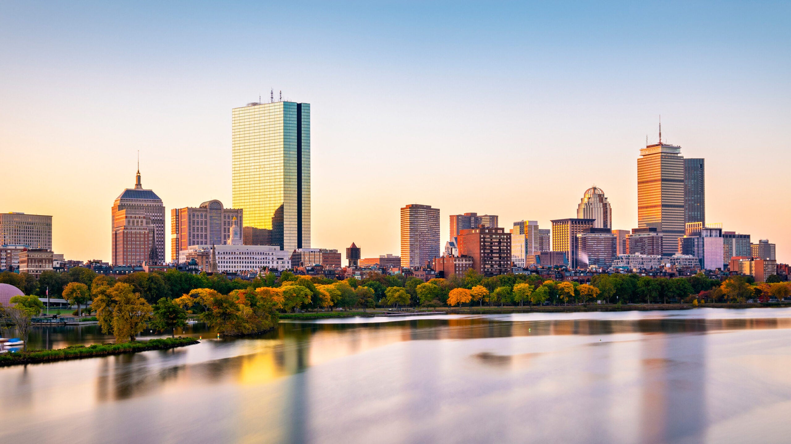 The skyline of Boston at sunset. The Charles river in front of the buildings reflects them onto the water. 