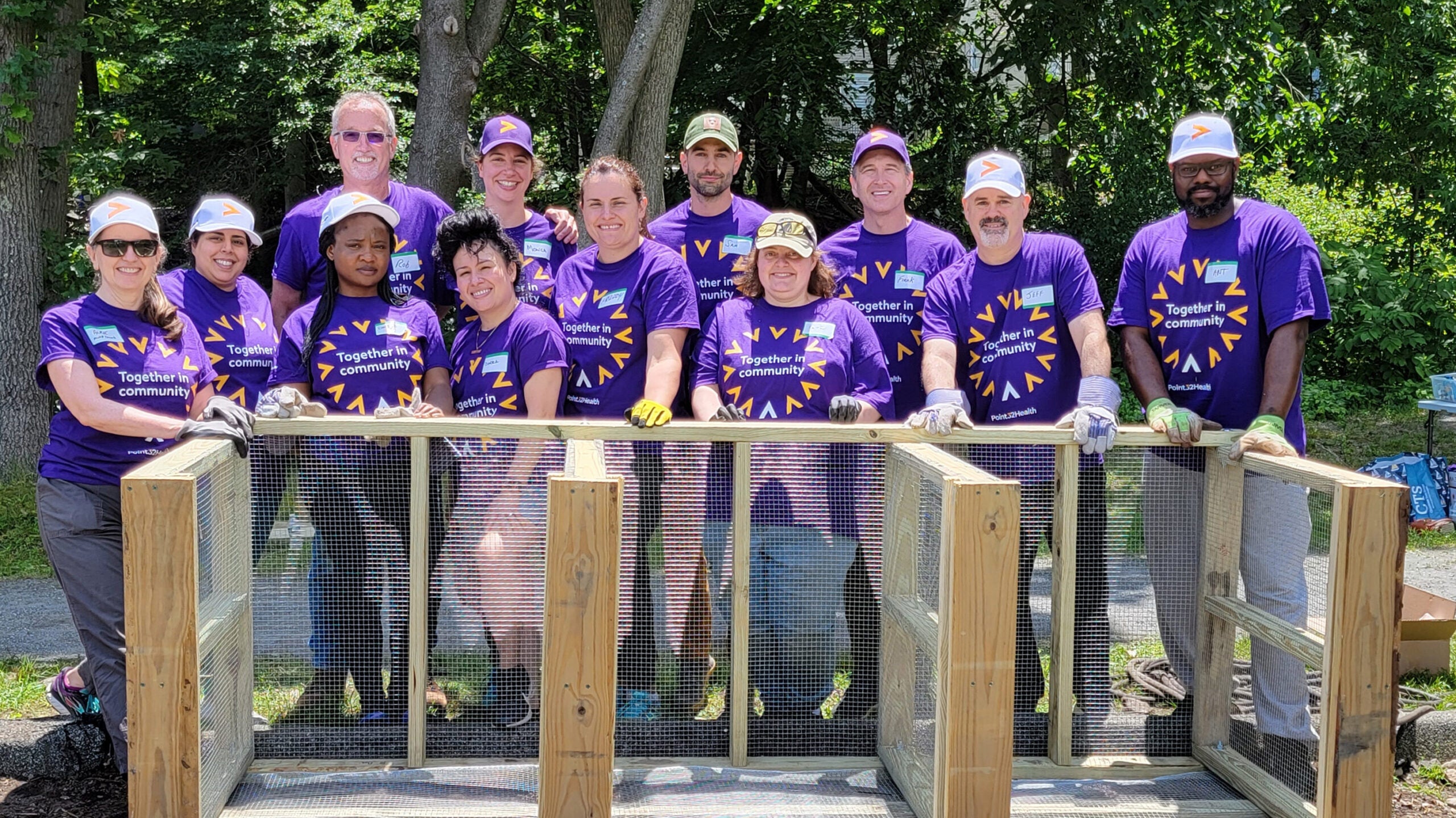 Twelve volunteers wear matching purple shirts as they stand around  wooden blocks.