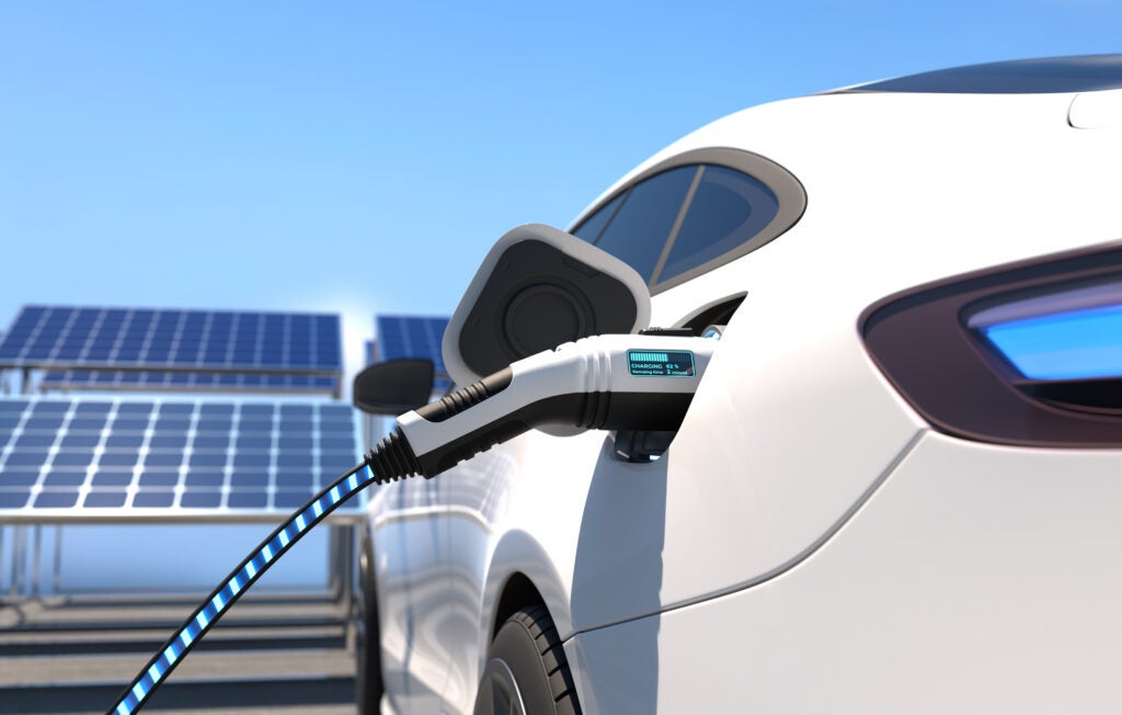 An electric car parked next to a set of solar panels is charged using clean energy filling technology 