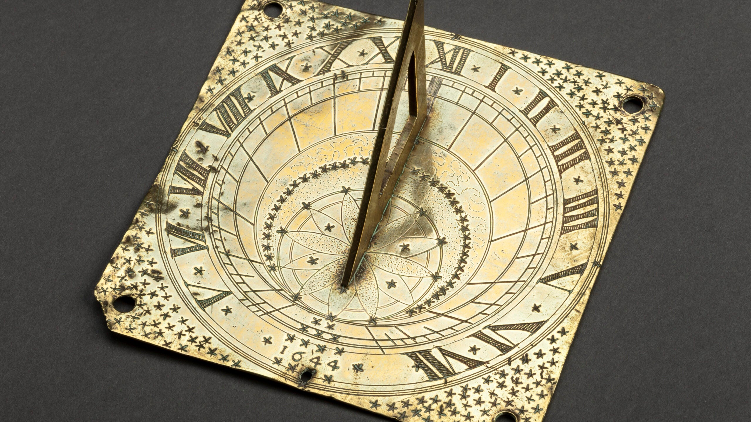 A gold sundial with roman numerals and stars from the Peabody Essex Museum sits on a grey background.