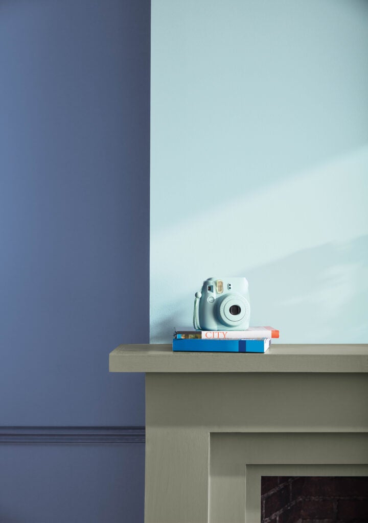 A back wall in Blue Nova 825 highlights a light blue polaroid camera sitting atop two books. Beneath the books sits a fire place, the trim of which is painted in antique pewter. 