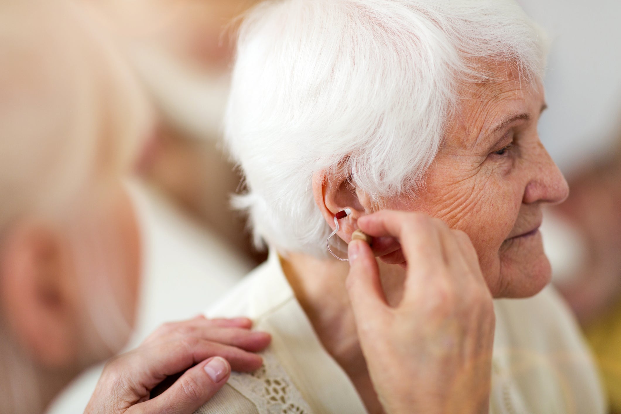 A female doctor applies a hearing aid to a senior woman's ear. 