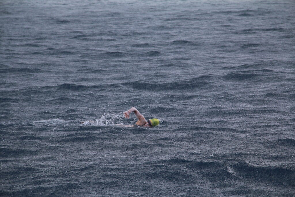 Sydne Didier swimming in the middle of the ocean while wearing a swim cap and goggles. 