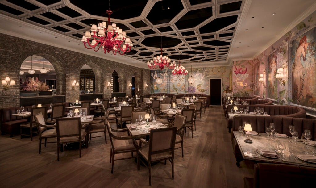 A french-inspired high-end restaurant with European wallpaper, pink chandeliers, and dim lighting. 