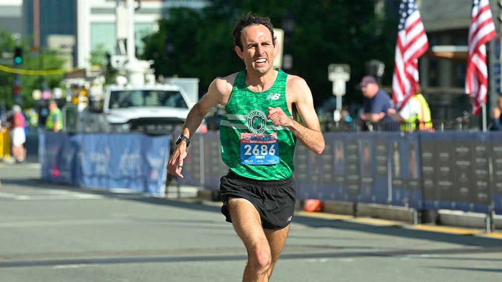 A man in a green tank top running a marathon on a closed down road.