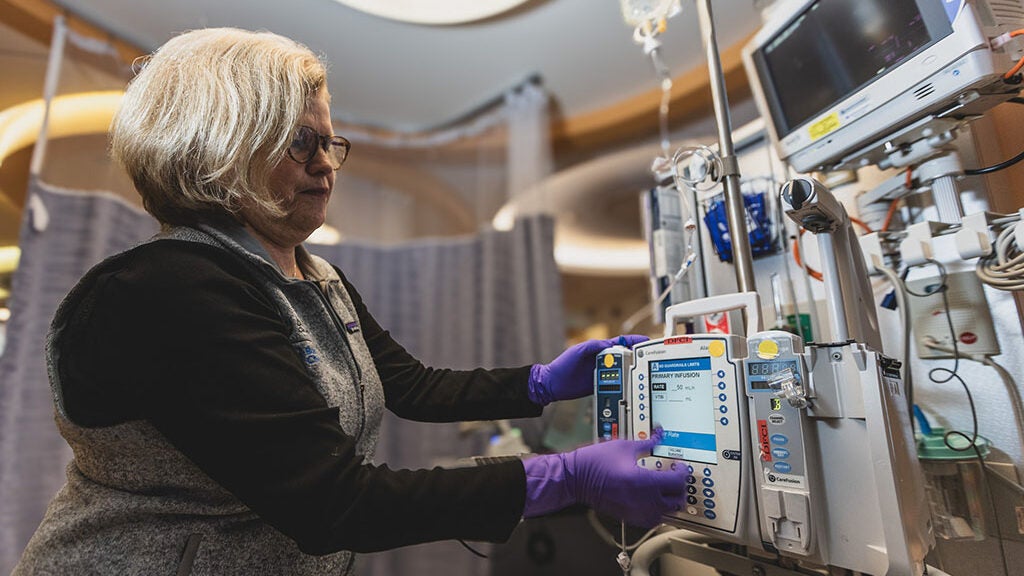 Woman wearing purple gloves adjusts a machine in a hospital