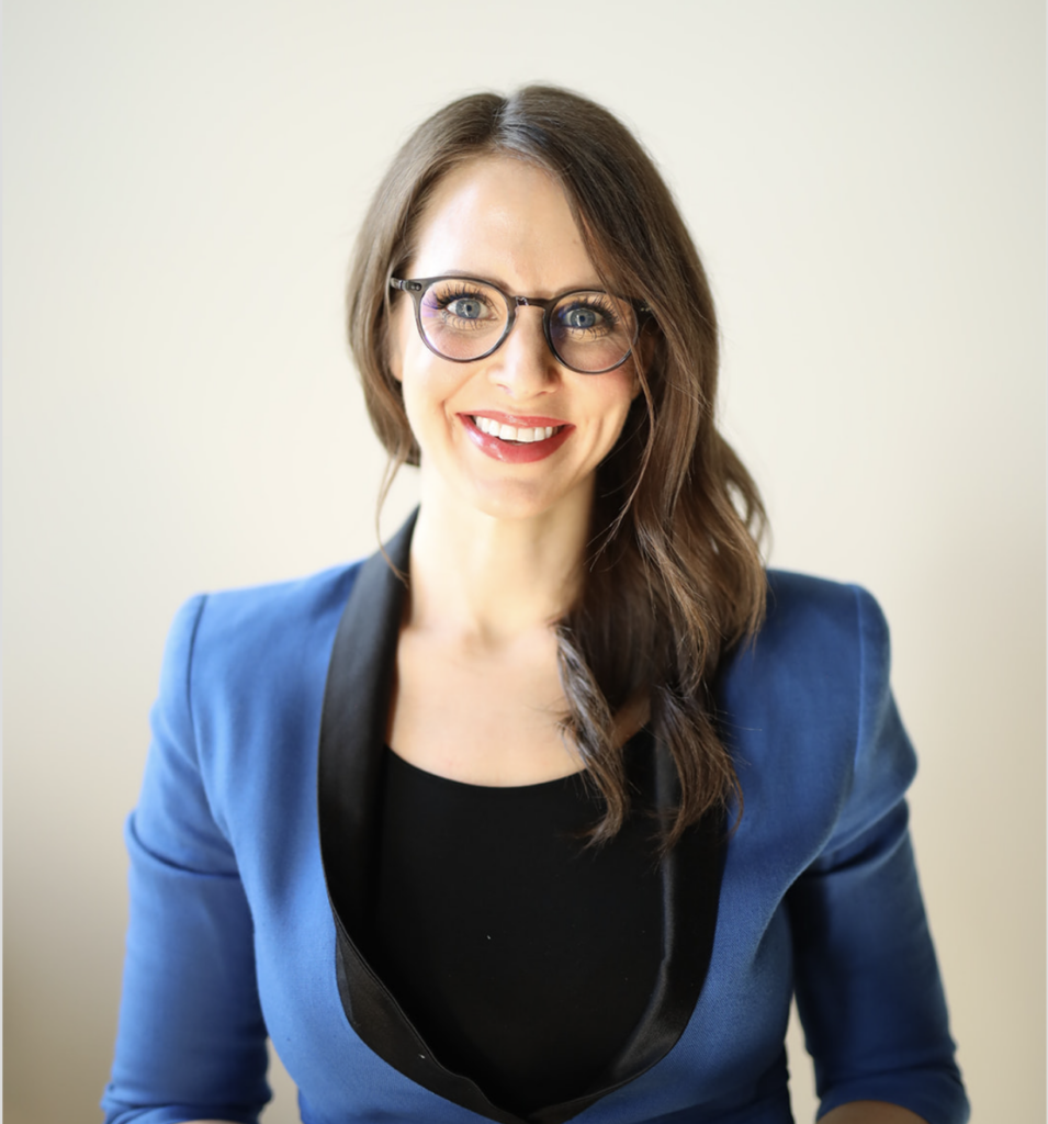 Headshot of a woman with long brown hair wearing glasses and a blue blazer.