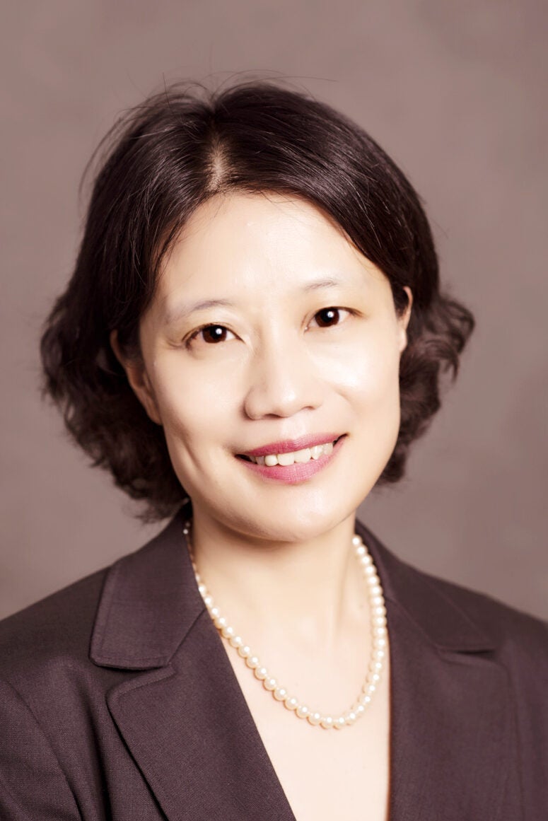 Zhang smiles at the camera with cropped brown hair. She wears a brown vest with a pearl necklace.