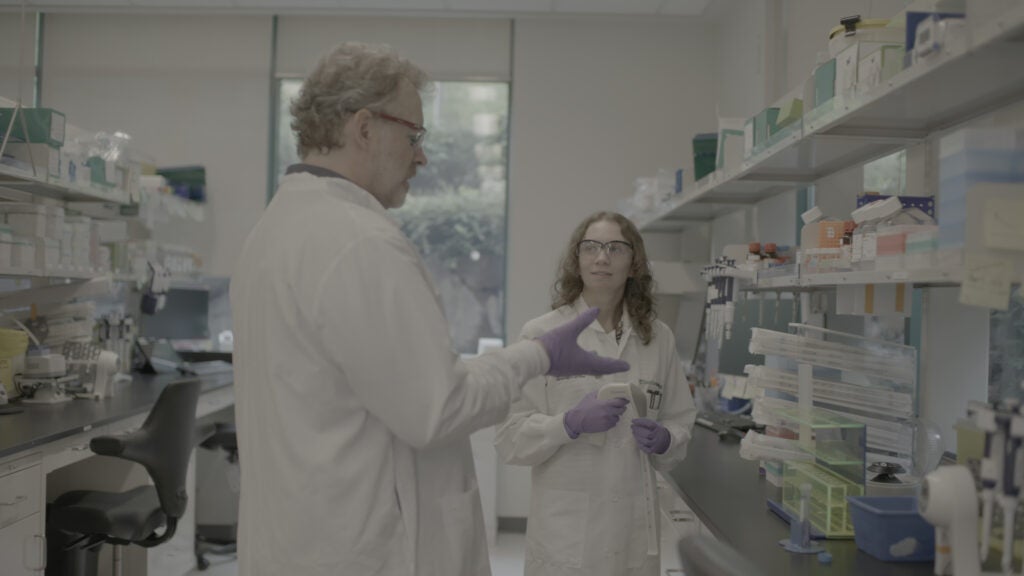 A man and woman wearing a white lab coat with glasses working in a science lab. 