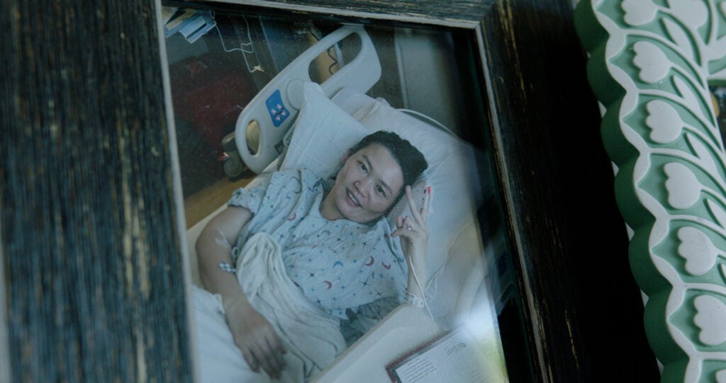 A framed, printed photo of a woman laying in a hospital bed holding up a "peace" sign with her hands.