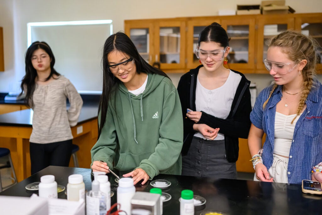 Girl wearing a green sweatshirt and lab goggles performing a scientific experiment 