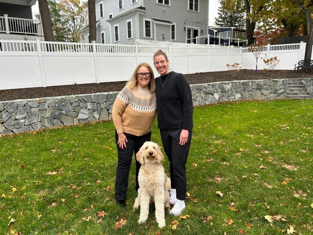 Two women smiling alongside their dog