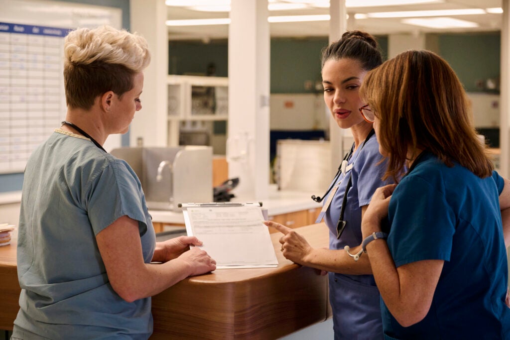 Three nurses gathered around the front desk chatting