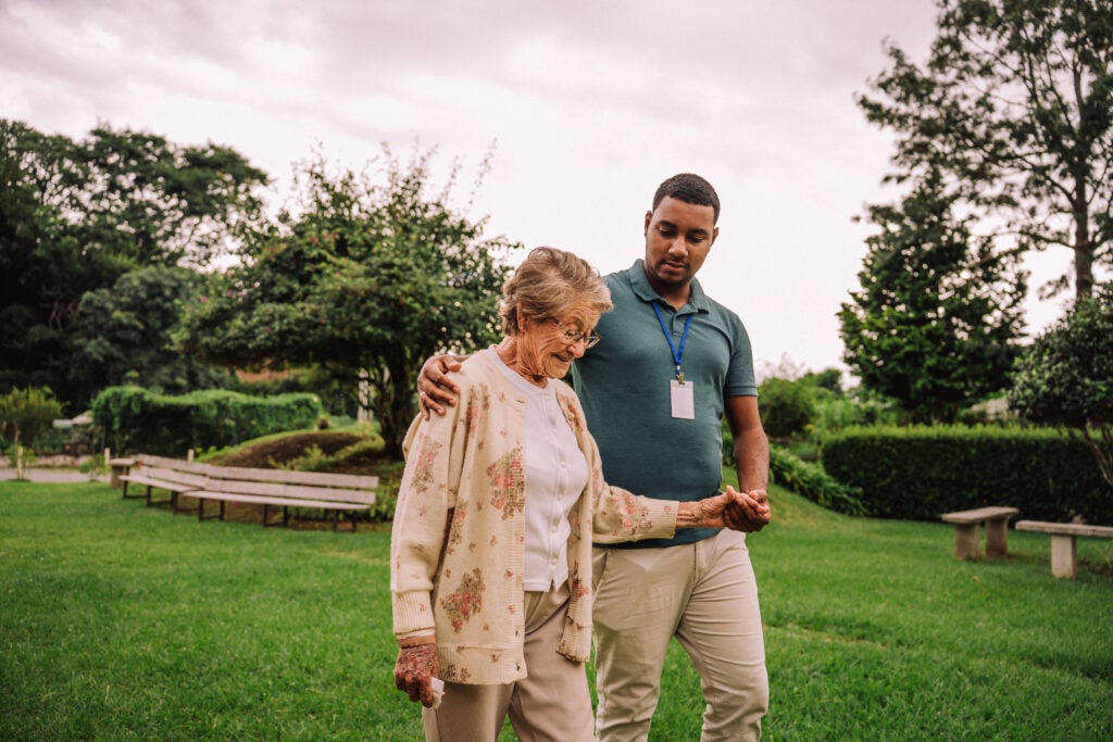 Nurse walks with patient in a park filled with trees